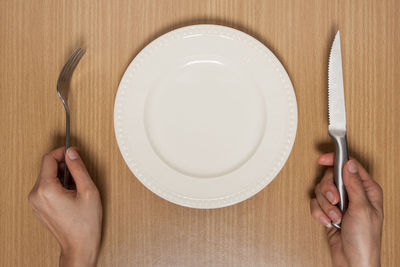 Cropped hands of woman by eating utensils over table