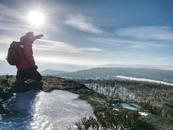 Man with raised arm on icy stone and looking on snow covered mountains. landscape with traveler