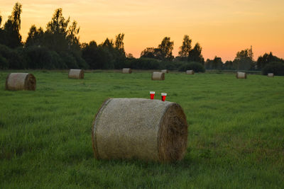 Hay bales on field against sky during sunset