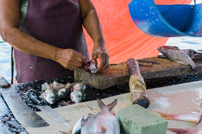 Midsection of woman cleaning fish on cutting board in market