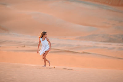 Woman standing on desert against sky during sunset