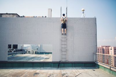 Rear view of man climbing ladder on rooftop