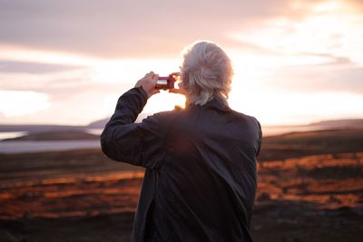 Woman standing by sea against sky during sunset