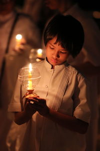 Girl holding illuminated candle while standing at night