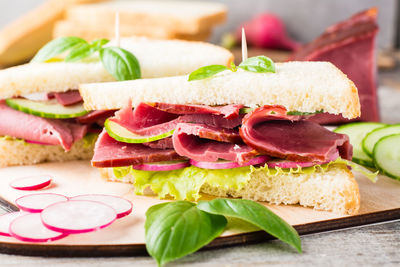 Fresh sandwiches with pastrami, cucumber, radish and basil on a cutting board