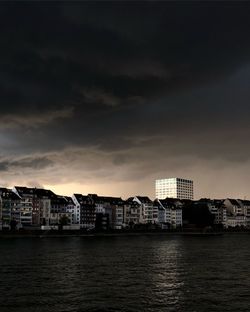 Sea by buildings against sky at dusk