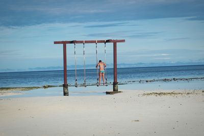 Rear view of woman in bikini standing on swing at shore of beach