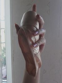 Cropped hand of woman holding ballet shoe at home