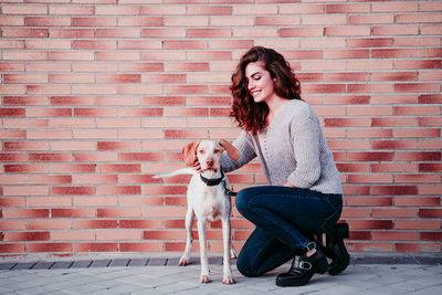 Smiling woman by dog against brick wall