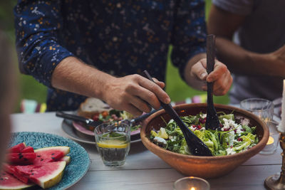 Midsection of man mixing salad at table during garden party