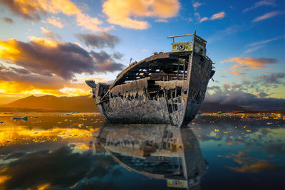 Abandoned boat moored in sea against sky during sunset