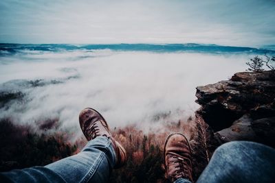 Low section of man sitting on cliff against sky