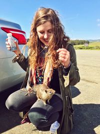 Young woman with squirrel crouching by car on road