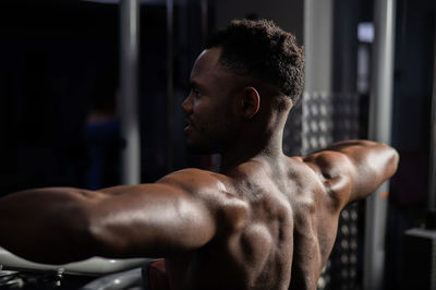 Shirtless african american man doing back exercises on a machine in the gym.