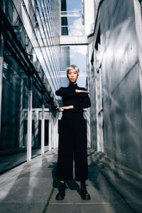 Portrait of smiling woman gesturing equal sing while standing against building