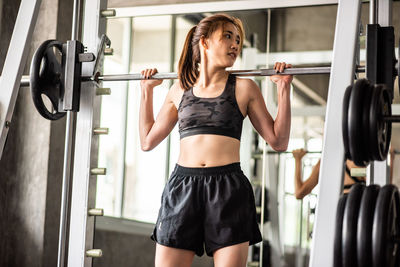 Young woman lifting weights while standing in gym