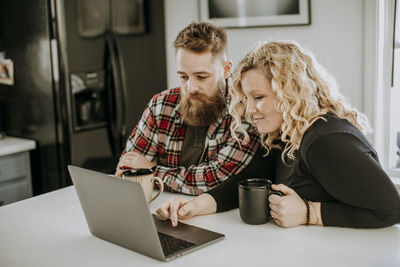 Man and woman couple sit in kitchen with laptop computer and coffee