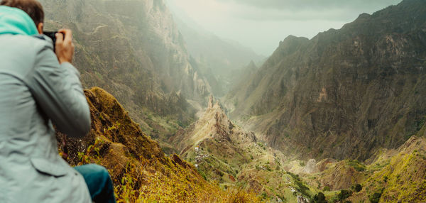 Rear view of man photographing while sitting on mountain