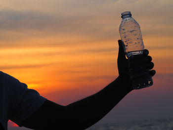 Cropped hand of man holding water bottle at beach during sunset