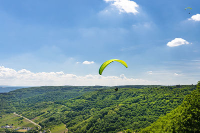 Man flying a green paraglider over beautiful wineries in germany, visible river and forest.