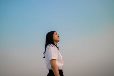 Young woman with eyes closed standing against sky during sunset