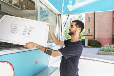 Side view of confident young male salesman holding menu placard at food truck