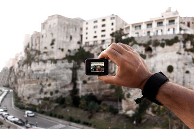 Midsection of man using mobile phone against buildings in city