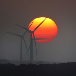 Silhouette of wind turbines on field against orange sky