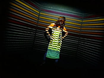 Full length of young woman standing against illuminated wall