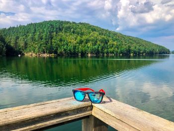Sunglasses with blue lenses on wooden fence with lake and green forest in the background
