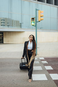 Young businesswoman with suitcase crossing street