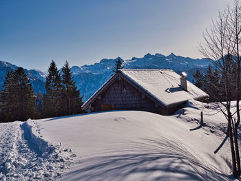 Snow covered houses by trees against sky