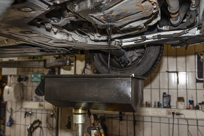 Draining used diesel engine oil from an oil pan into a metal container in a car workshop.