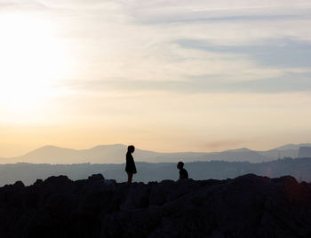 Silhouette couple on mountain against cloudy sky during sunset