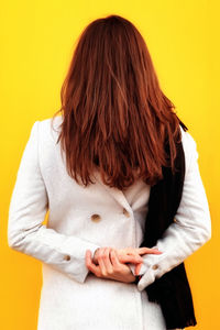 Rear view of woman with arms raised against yellow background