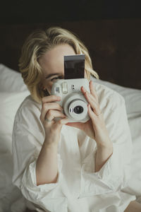 Blond woman photographing in bedroom