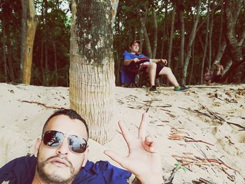 Portrait of happy friends sitting on tree trunk in forest