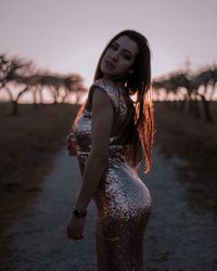 Portrait of young woman standing on field against sky