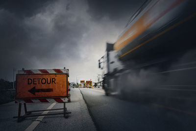 Road sign on street in city against sky