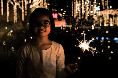 Portrait of smiling girl with sparkler in city at night