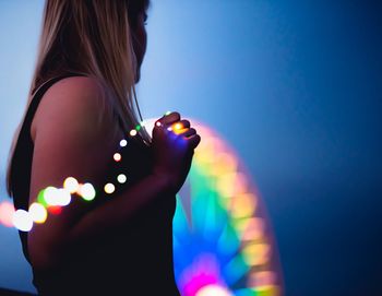 Close-up of woman standing by defocused lights at night