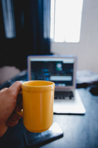 Midsection of person holding coffee cup on table at home