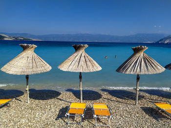 Deck chairs and parasols on beach against blue sky