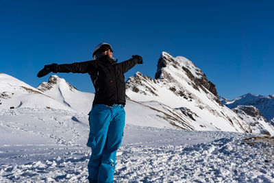 Man standing on snowcapped mountain against blue sky