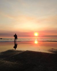 Silhouette man standing on beach against sky during sunset