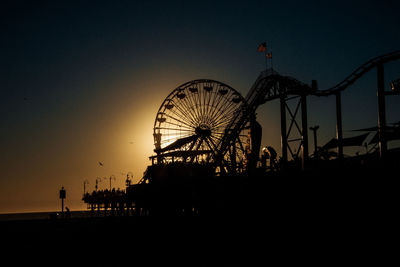 Silhouette ferris wheel at beach against clear sky