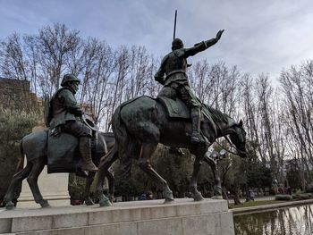 Statue by bare trees against sky