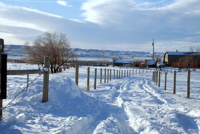 Fence on snow covered field against sky