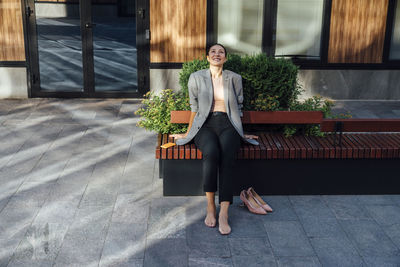 Smiling thoughtful businesswoman sitting on bench at office park