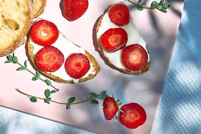 Toast bread with spread stracchino cheese and slices of ripe red strawberry on pink plate